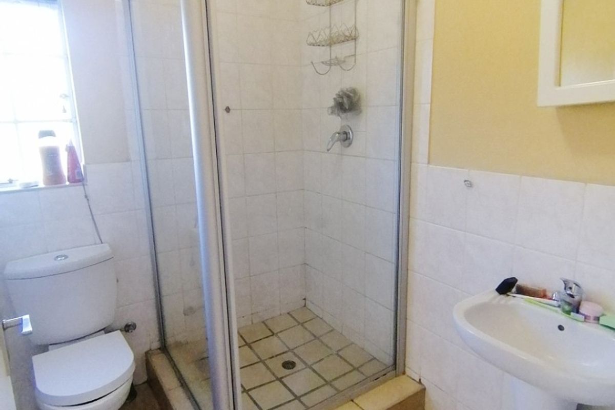 A functional bathroom featuring a shower enclosure, pedestal basin, and toilet with tiled finishes throughout.