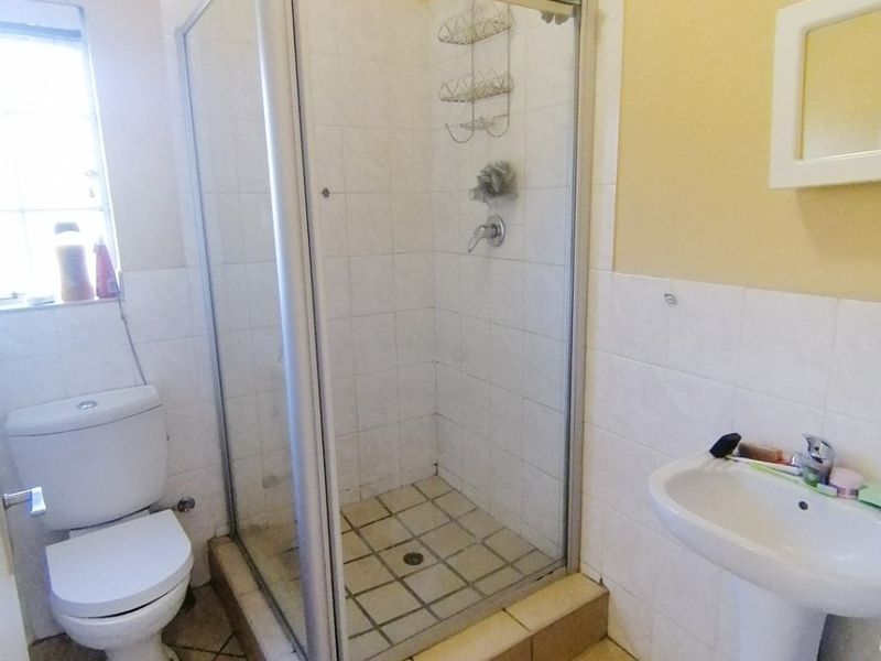A functional bathroom featuring a shower enclosure, pedestal basin, and toilet with tiled finishes throughout.