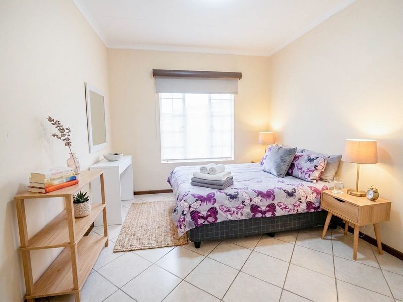 A well-lit bedroom featuring neutral wall tones, tiled flooring, and a window with a roller blind, providing a clean and functional living space.