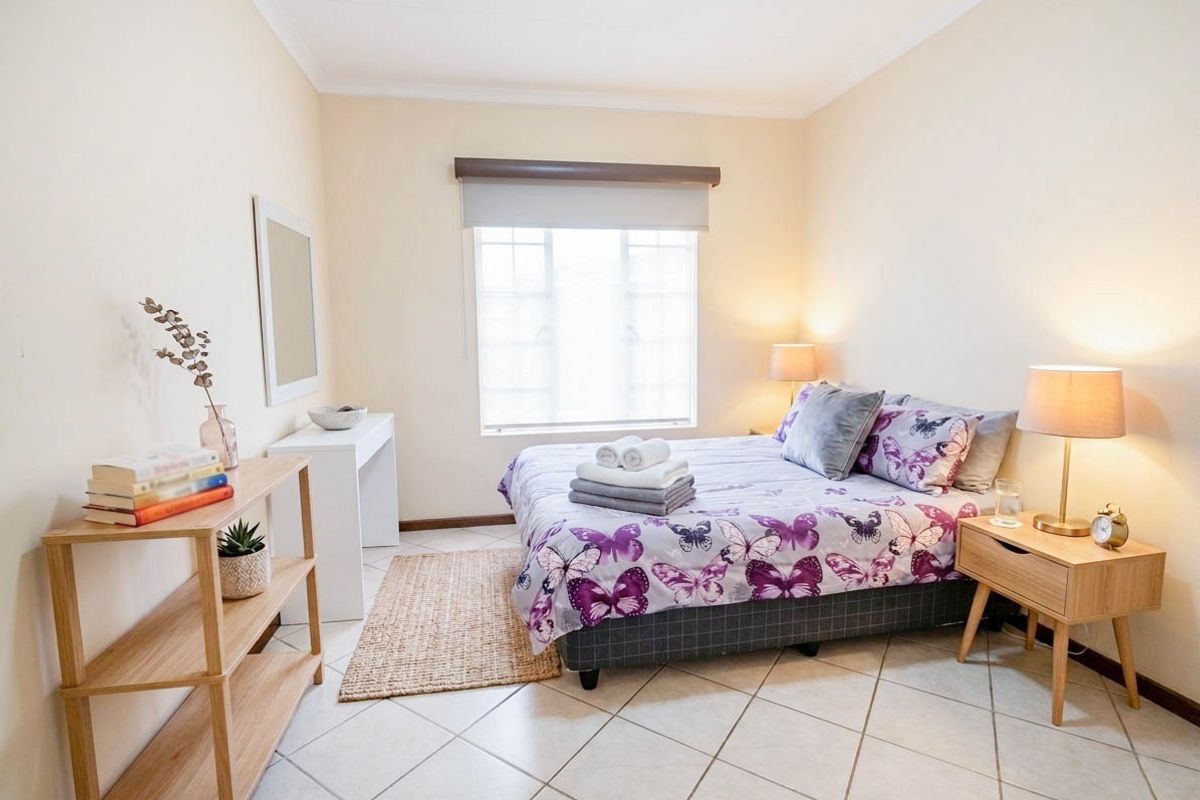 A well-lit bedroom featuring neutral wall tones, tiled flooring, and a window with a roller blind, providing a clean and functional living space.