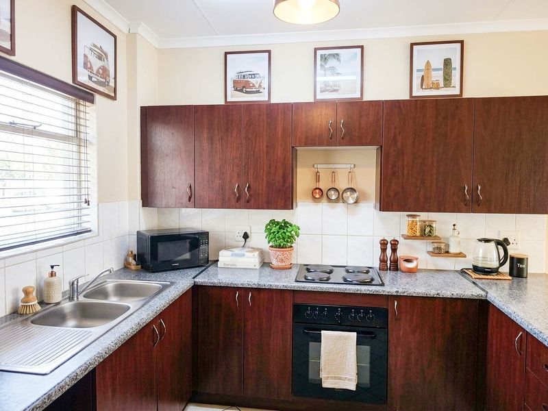 A functional kitchen featuring dark wood-look cabinetry, granite countertops, a double stainless steel sink, and built-in electric cooking appliances with a tiled backsplash.