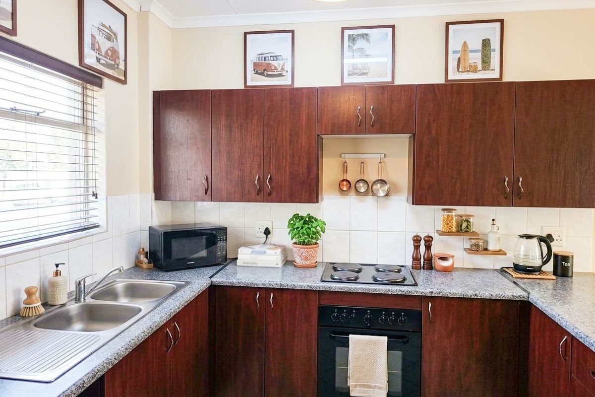 A functional kitchen featuring dark wood-look cabinetry, granite countertops, a double stainless steel sink, and built-in electric cooking appliances with a tiled backsplash.