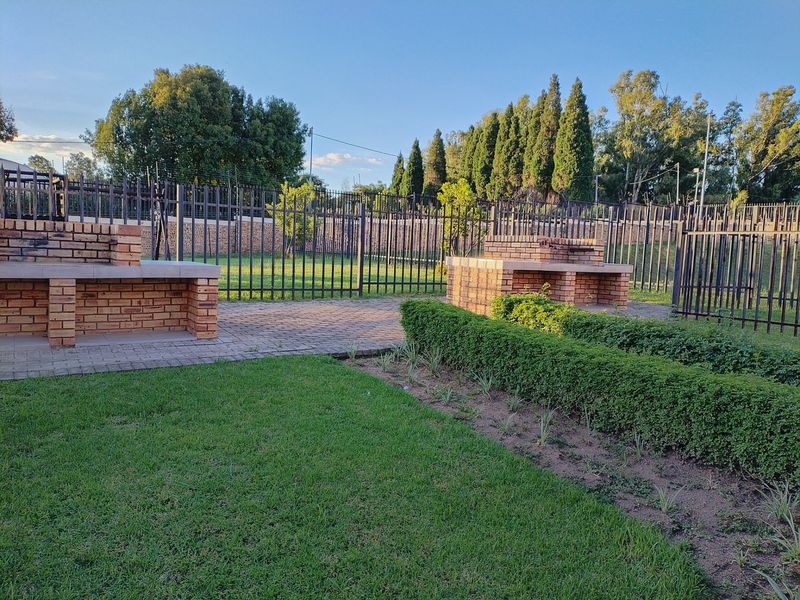 A well-maintained communal garden area featuring brick built-in braai facilities, paved walkways, and secure perimeter fencing.