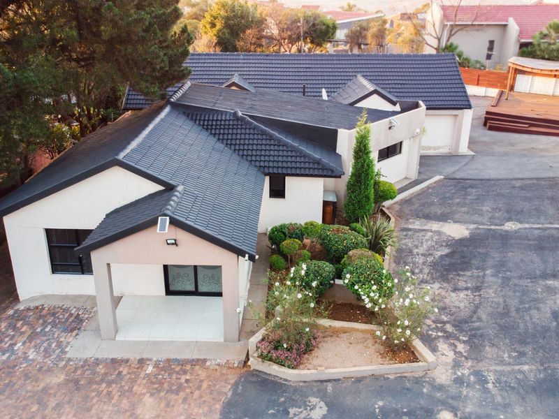 Aerial view of a residential property featuring a tiled roof, paved driveway, covered entrance, double garage, and a raised timber deck in the rear garden.