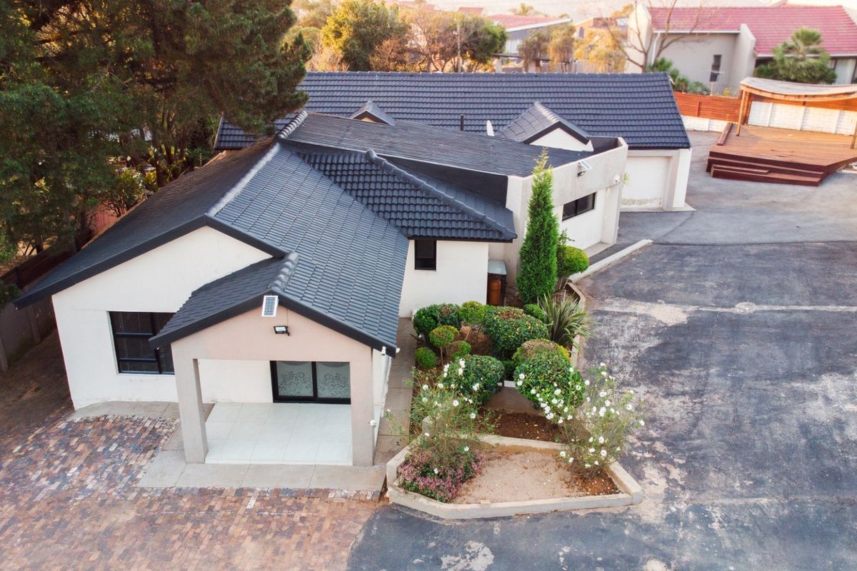 Aerial view of a residential property featuring a tiled roof, paved driveway, covered entrance, double garage, and a raised timber deck in the rear garden.