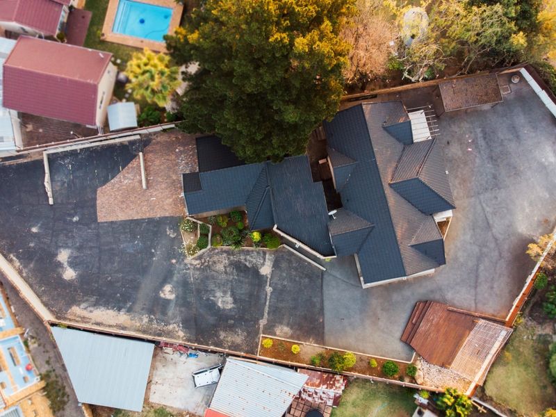 Aerial view of the property showcasing the roof structure, extensive paved driveway, and a wooden deck area within the boundary.
