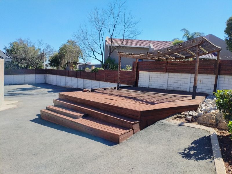 Outdoor timber deck area featuring a wooden pergola, set within a paved backyard with perimeter boundary walls and fencing.