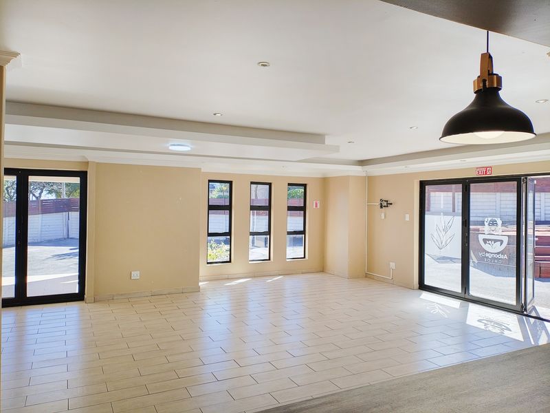 Spacious open-plan living area featuring neutral tiled flooring, modern recessed lighting, and large aluminium-framed glass doors providing ample natural light and outdoor access.