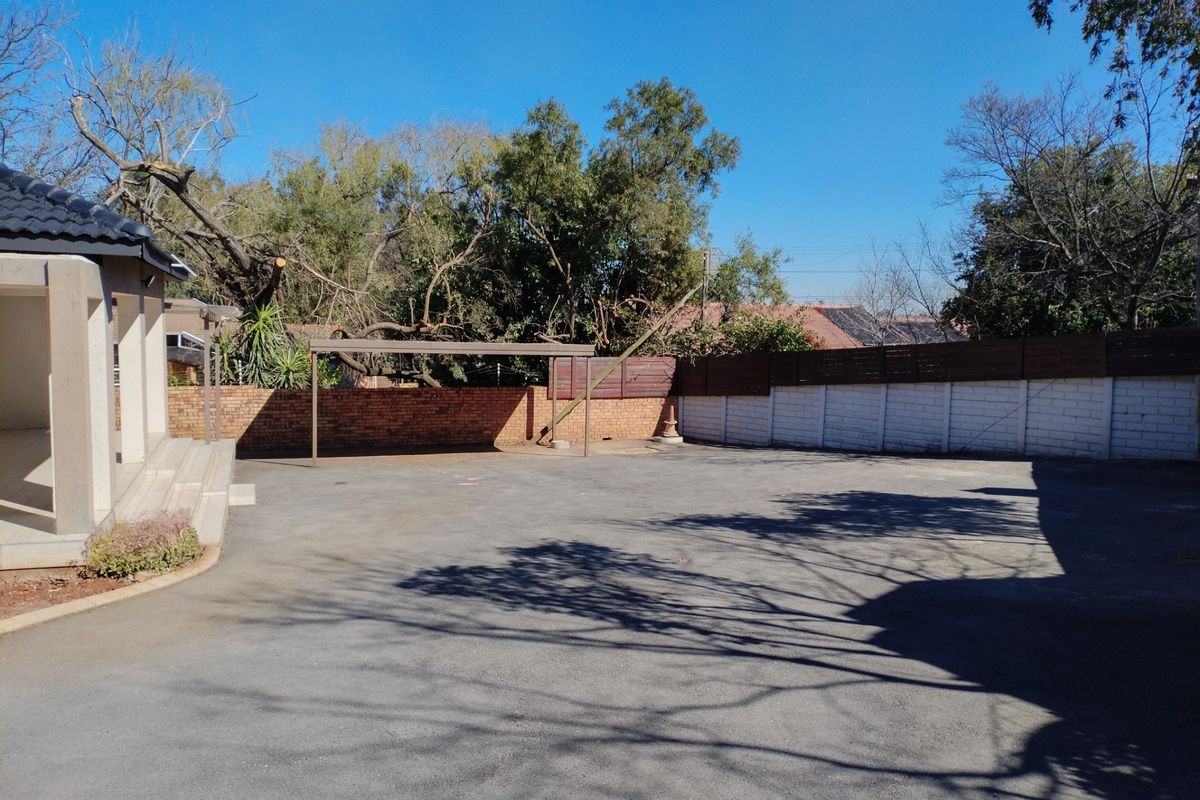 Spacious rear exterior area featuring a paved driveway, covered patio, and brick boundary wall, providing ample outdoor space.