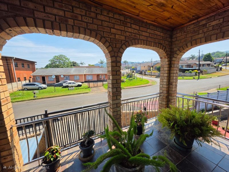 A covered balcony featuring brick arches, a timber ceiling, and a metal balustrade, offering an elevated view of the surrounding residential street.
