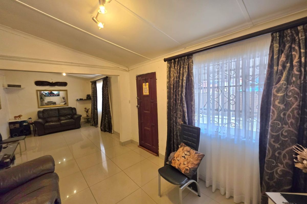 A living room featuring tiled flooring, track lighting, and a secure entrance door with window security bars.