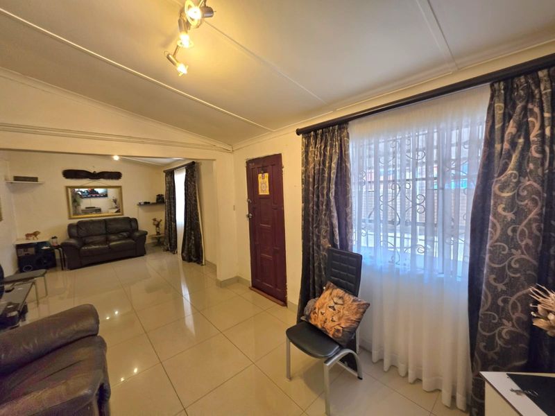 A living room featuring tiled flooring, track lighting, and a secure entrance door with window security bars.