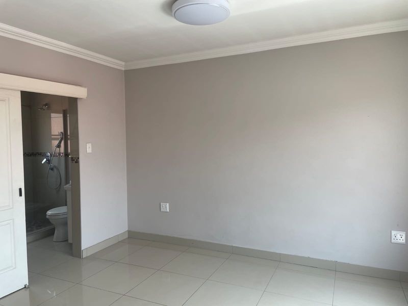 A clean, empty bedroom featuring neutral walls, tiled flooring, and an adjoining en-suite bathroom with a sliding door entrance.
