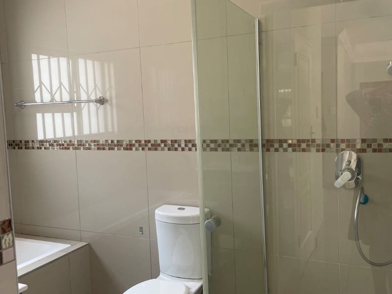 A clean, modern bathroom featuring a glass-enclosed shower, built-in bathtub, and neutral wall tiling with a decorative mosaic border.