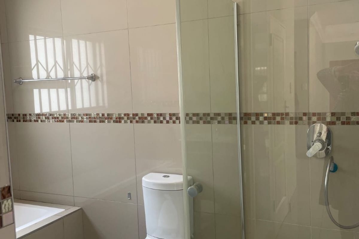 A clean, modern bathroom featuring a glass-enclosed shower, built-in bathtub, and neutral wall tiling with a decorative mosaic border.