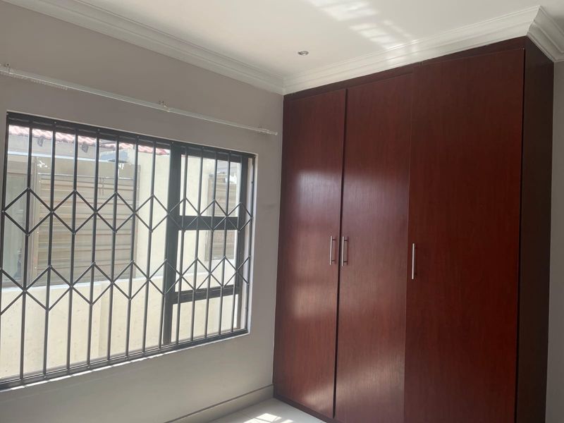 A clean, empty bedroom featuring dark wood built-in cupboards, a window with a security gate, and neutral wall finishes.