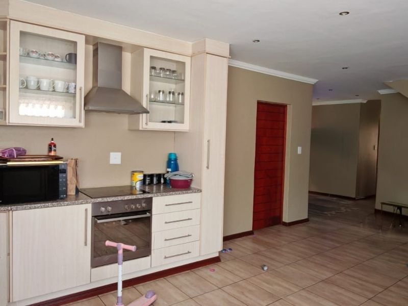 Open plan kitchen area featuring light wood cabinetry, integrated appliances, and tiled flooring, seamlessly flowing into the living space with an adjacent staircase.