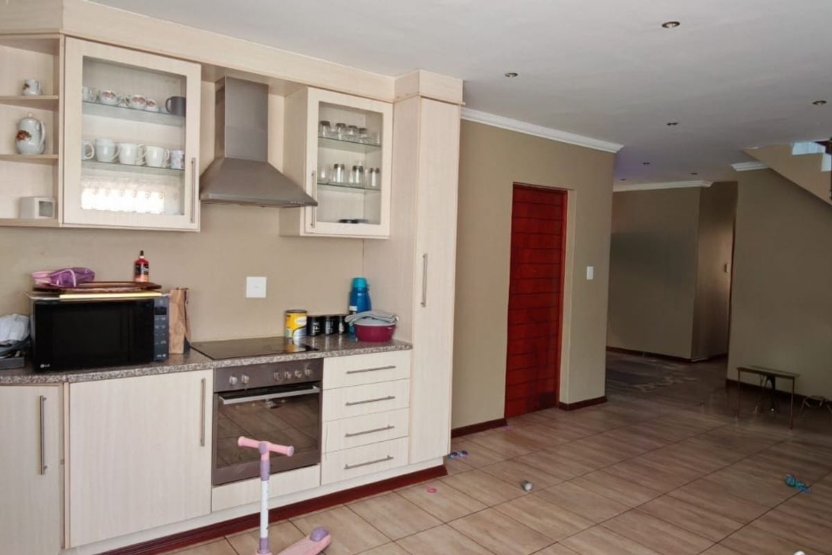 Open plan kitchen area featuring light wood cabinetry, integrated appliances, and tiled flooring, seamlessly flowing into the living space with an adjacent staircase.