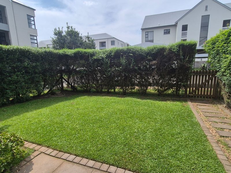 A well-maintained private garden featuring a manicured lawn, established perimeter hedging, paved pathways, and a secure timber gate.