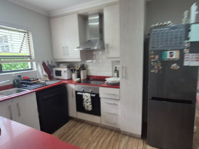 A functional kitchen featuring white cabinetry, a red countertop, subway tile backsplash, and integrated stainless steel appliances, including an oven and extractor fan.