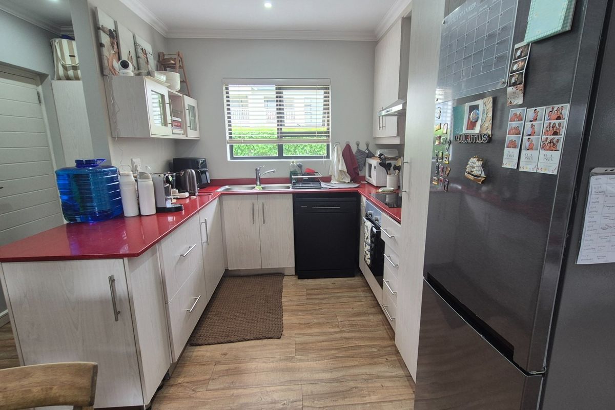 A functional kitchen featuring light wood-look cabinetry, contrasting red countertops, integrated oven, and wood-style laminate flooring with a window for natural light.