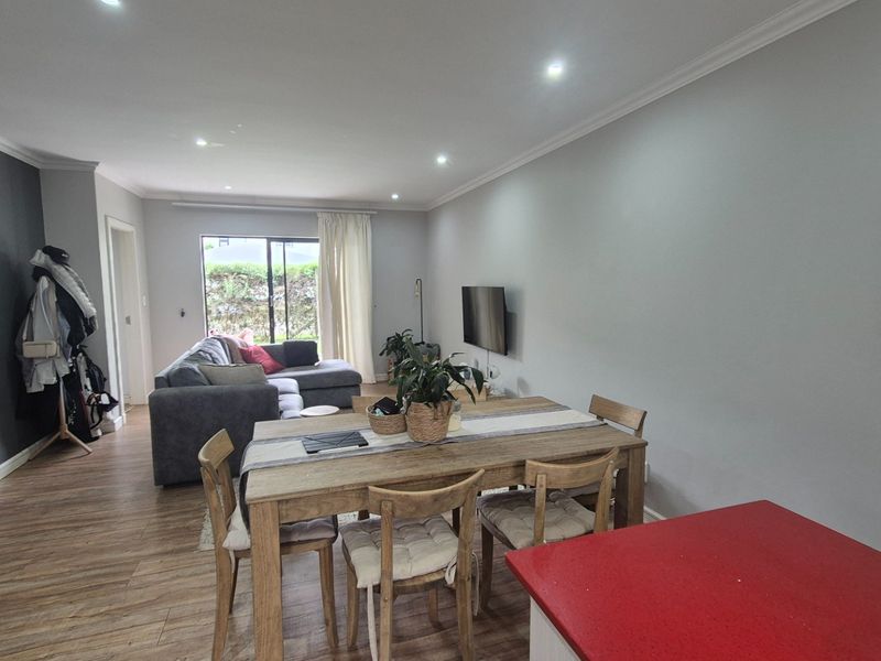 Spacious open-plan living and dining area featuring modern laminate flooring, recessed downlighting, and a kitchen island with a vibrant red countertop.