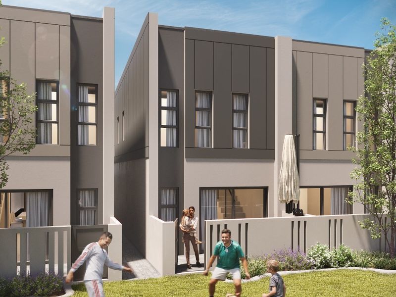 A modern rear exterior view of a townhouse development featuring a private patio and landscaped garden area.