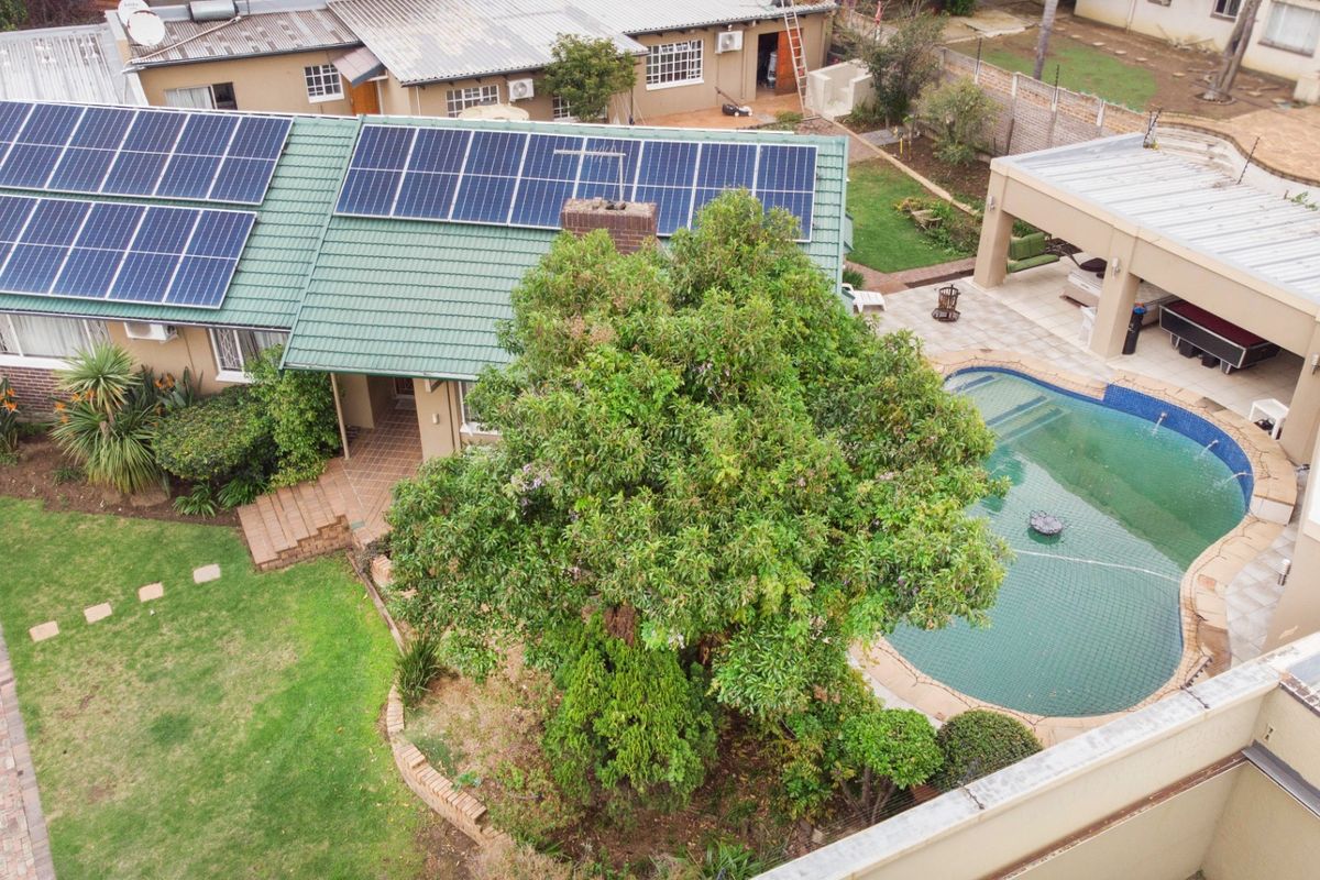 Aerial view of a residential property featuring a tiled roof with solar panels, a swimming pool, and a covered patio area.