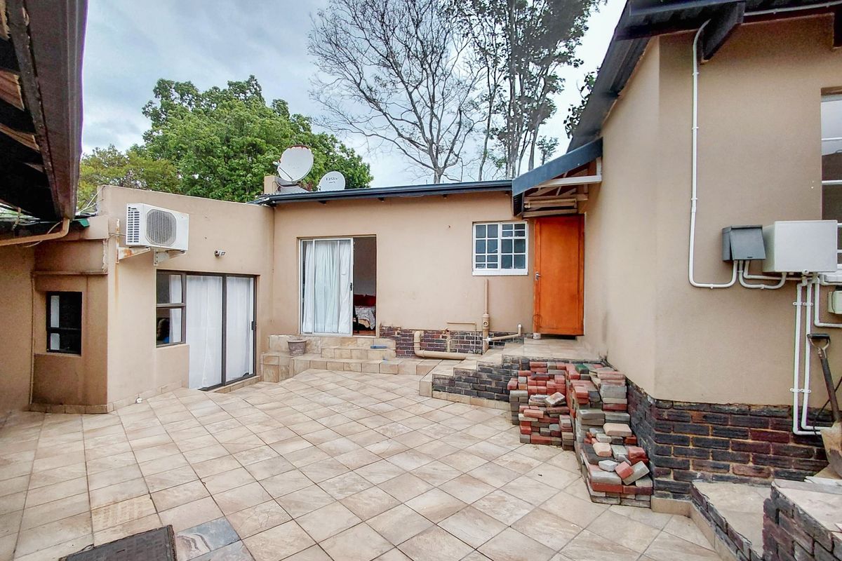 Rear exterior patio area featuring tiled flooring, sliding door access, and wall-mounted air conditioning unit, requiring some maintenance and cosmetic updates.