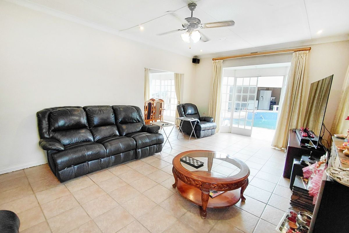 Spacious living room featuring tiled flooring, a ceiling fan, and large french doors providing direct access to the outdoor pool area.