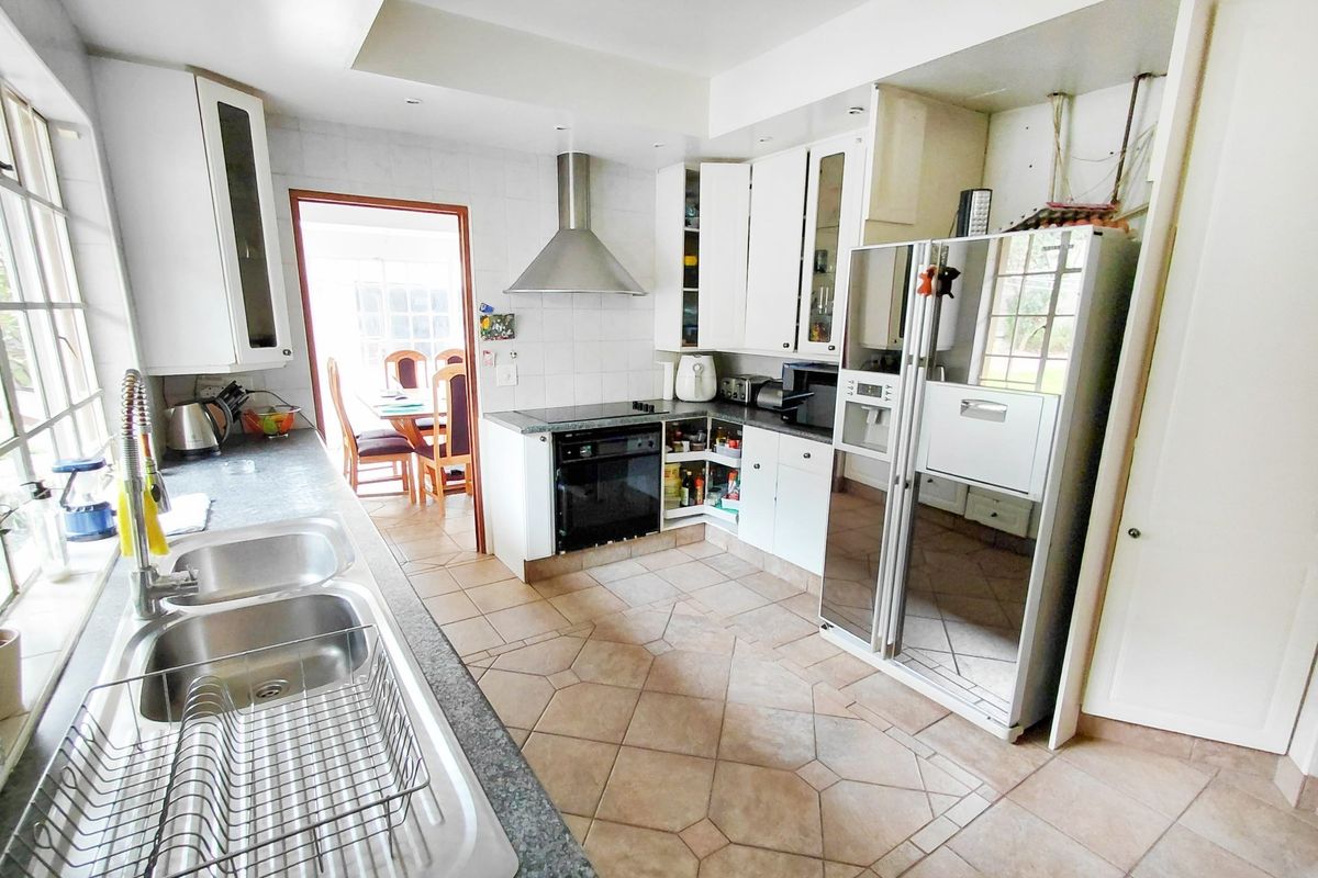 Functional kitchen featuring tiled flooring, built-in cabinetry, a double stainless steel sink, and integrated cooking appliances with an extractor fan.