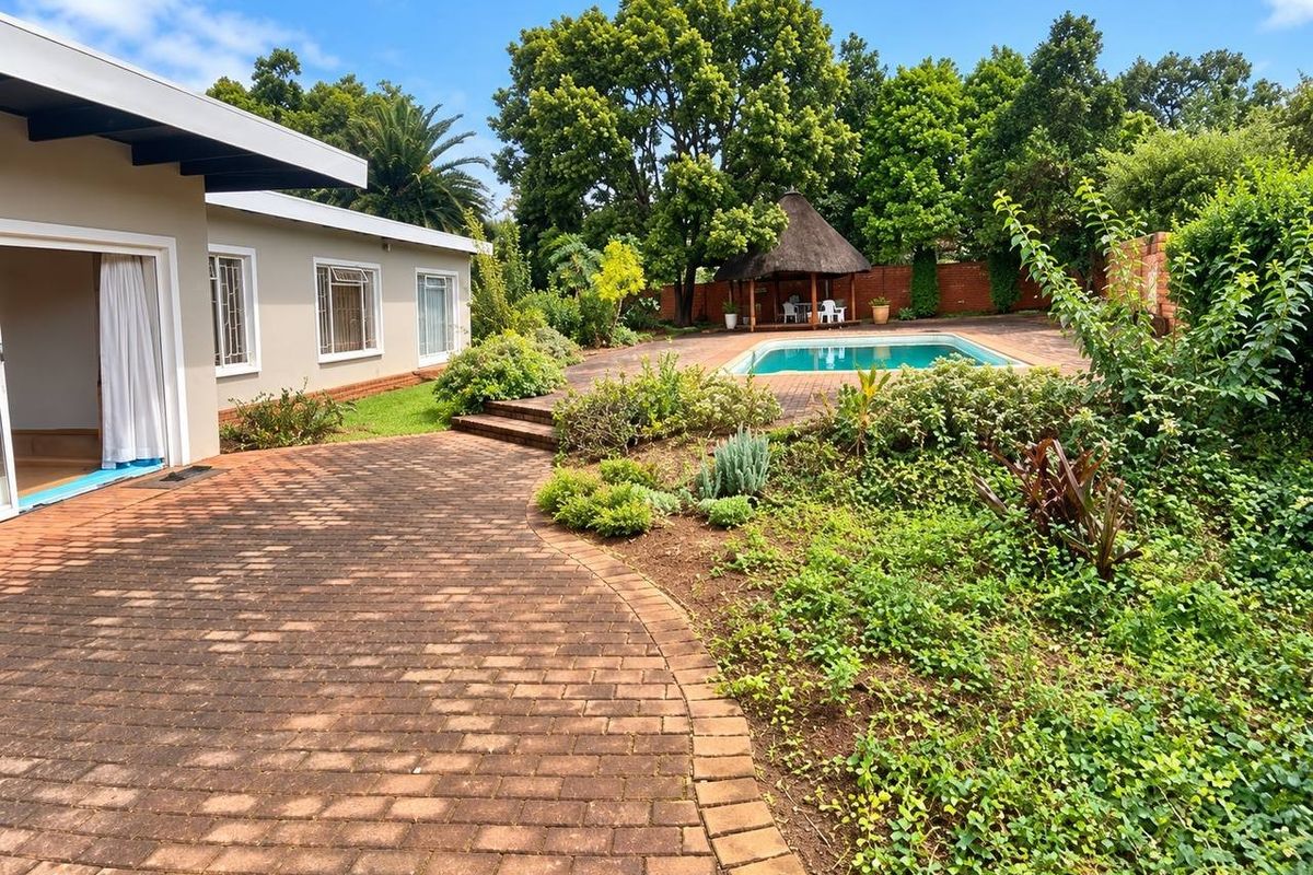 Spacious rear garden featuring a swimming pool, a thatched gazebo, and extensive brick paving, providing an ideal outdoor entertainment area.