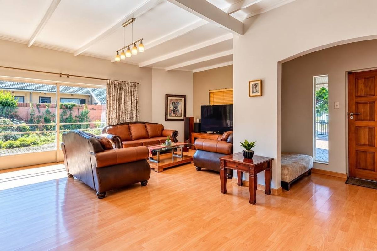 Spacious living room featuring laminate flooring, exposed beam ceilings, and a large sliding glass door providing natural light and access to the garden.