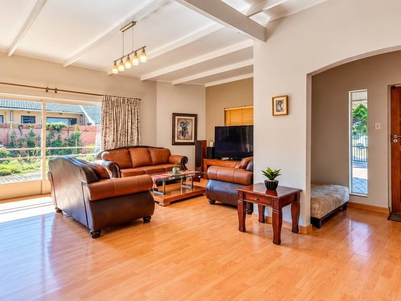 Spacious living room featuring laminate flooring, exposed beam ceilings, and a large sliding glass door providing natural light and access to the garden.