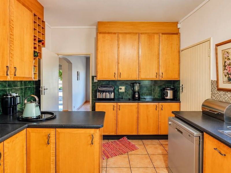 A functional kitchen featuring wooden cabinetry, dark laminate countertops, tiled backsplash, and tiled flooring, offering a classic and practical layout.