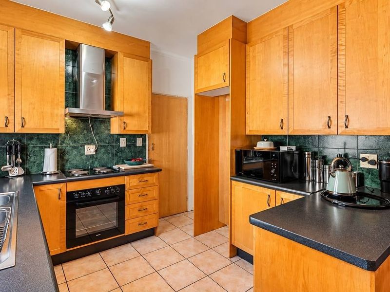 A functional kitchen featuring wooden cabinetry, dark laminate countertops, a tiled backsplash, and integrated appliances including an oven and extractor fan.