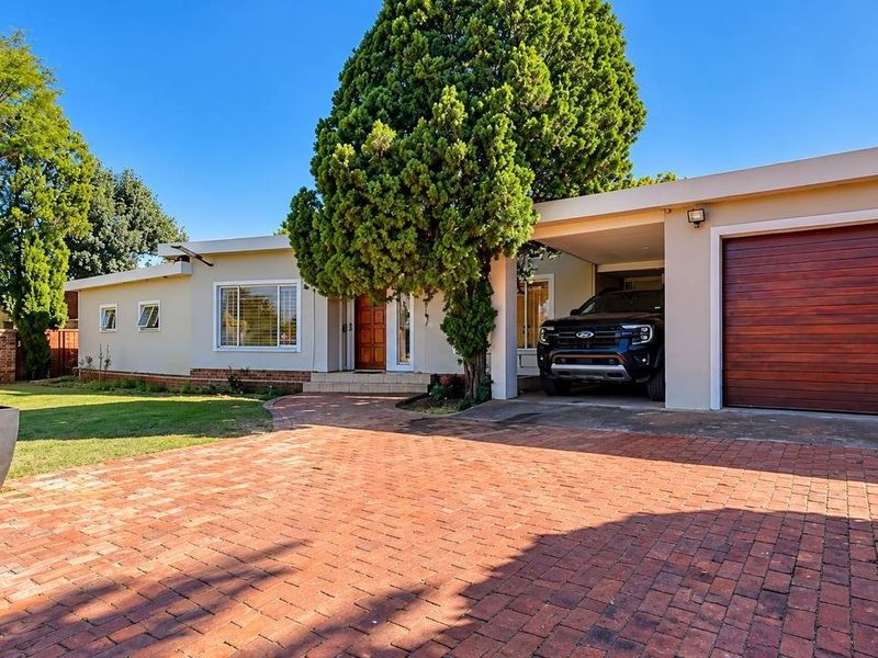 A well-maintained single-story home featuring a brick-paved driveway, a covered carport, and a prominent wooden garage door set within a landscaped front garden.