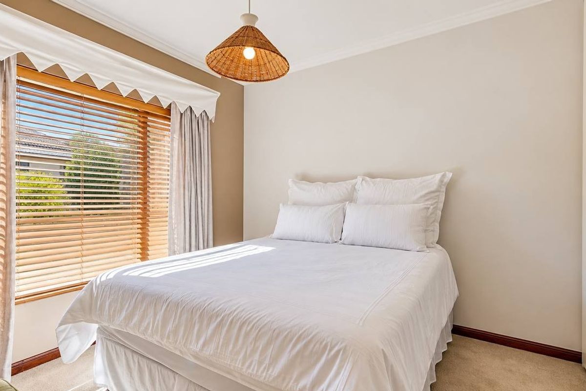 A bright and well-maintained bedroom featuring neutral walls, carpet flooring, built-in wardrobes, and timber venetian blinds allowing for natural light.
