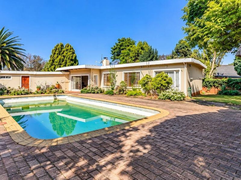 Spacious rear garden featuring a swimming pool, paved patio area, and a traditional thatch lapa, perfect for outdoor entertaining.