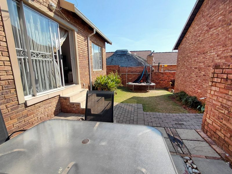 A rear exterior view of the townhouse featuring a brick facade, a paved patio area, and a small private garden with boundary walls.