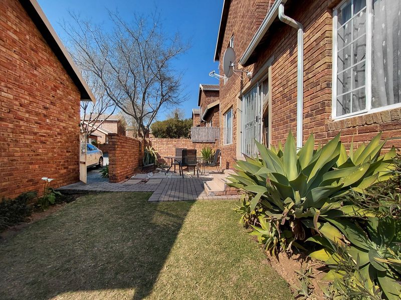 A private rear courtyard featuring a paved patio area, established lawn, and brick boundary walls, accessible via a sliding glass door.