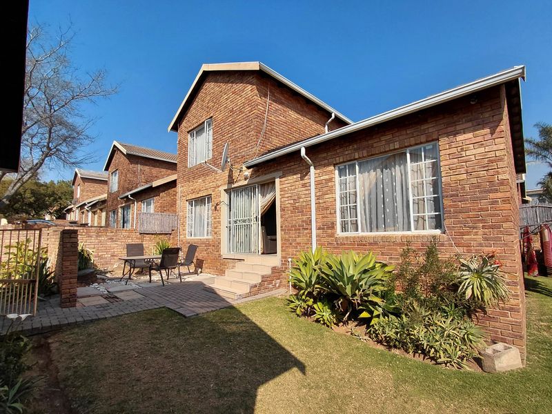 Rear view of a double-story face brick townhouse featuring a paved patio area, garden space, and sliding door access.