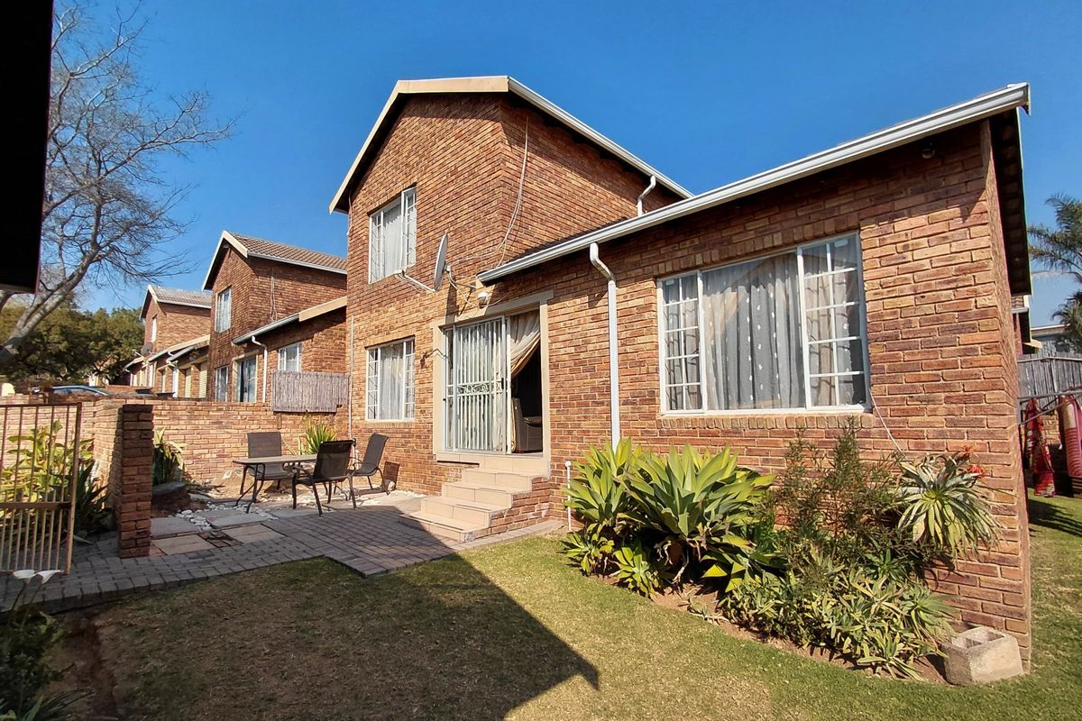 Rear view of a double-story face brick townhouse featuring a paved patio area, garden space, and sliding door access.