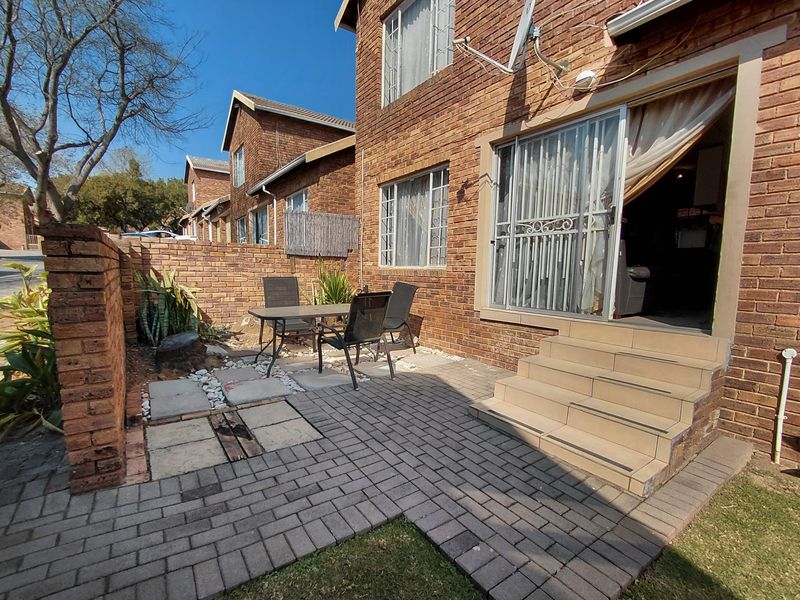 A private paved patio area featuring brick boundary walls, tiled steps leading to a sliding glass door, and direct access to the townhouse interior.