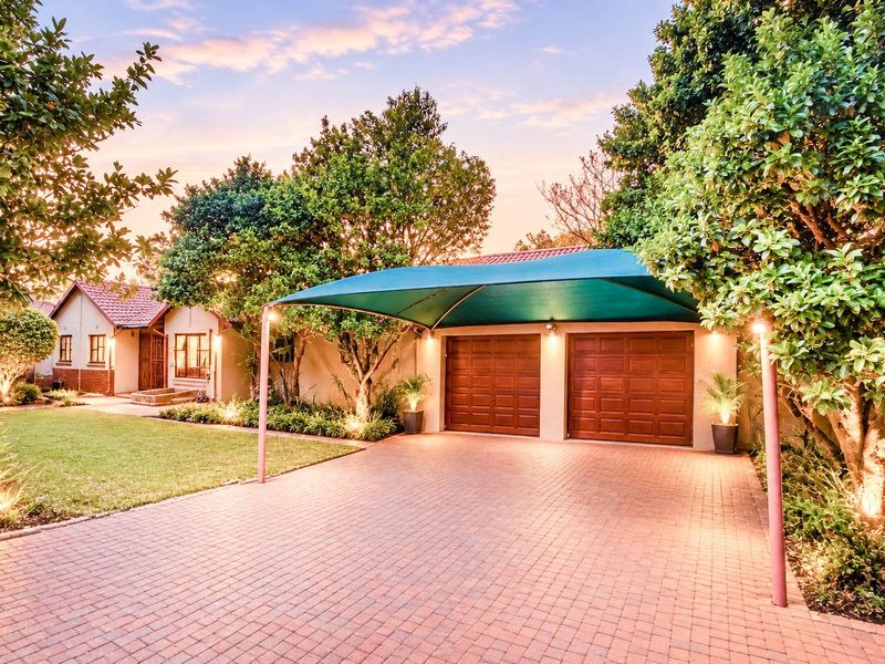Front view of the property featuring a paved driveway, double garage with a shade sail, and a well-maintained landscaped garden with exterior lighting.