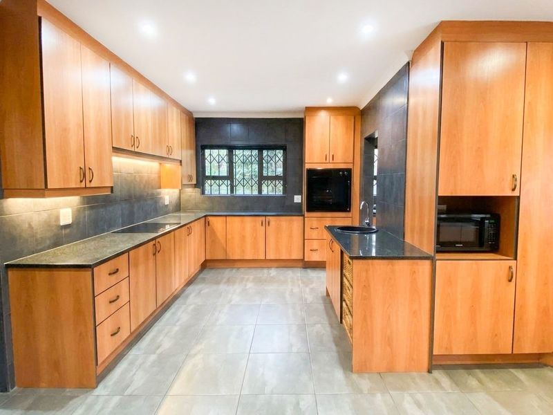 A spacious, well-maintained kitchen featuring warm wood-toned cabinetry, dark granite countertops, integrated appliances, and modern recessed lighting.