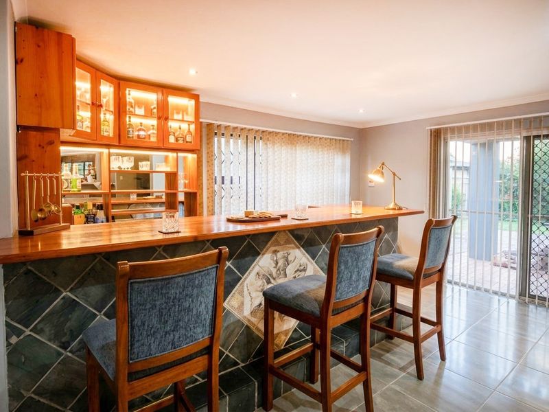 A dedicated home bar area featuring a built-in wooden counter, tiled front, integrated cabinetry with display lighting, and direct access to the patio.