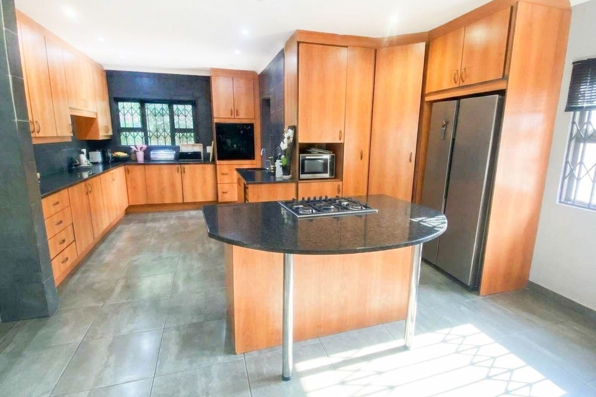 Spacious kitchen featuring extensive wooden cabinetry, granite countertops, a central island with a gas hob, and tiled flooring throughout.