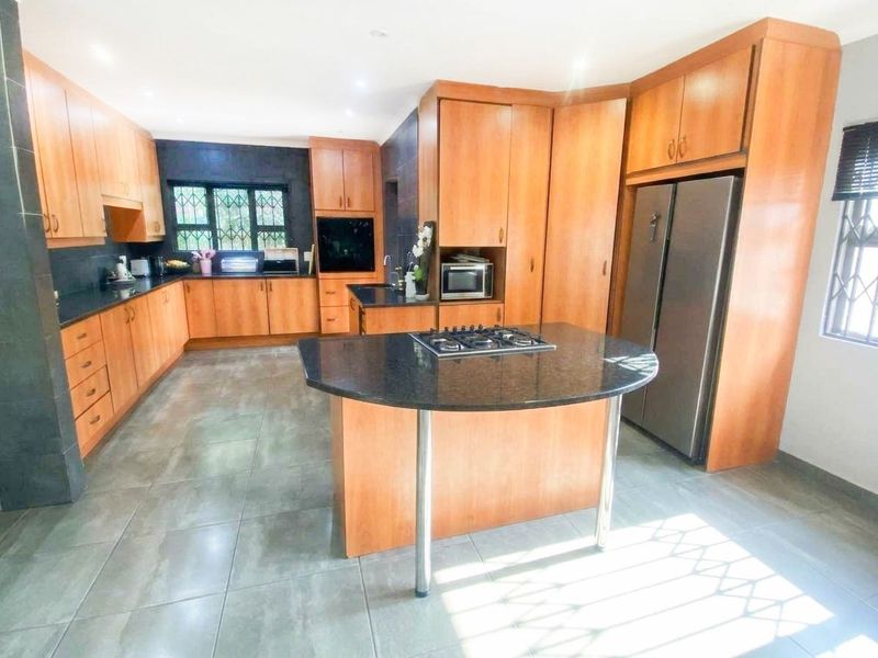 Spacious kitchen featuring extensive wooden cabinetry, granite countertops, a central island with a gas hob, and tiled flooring throughout.