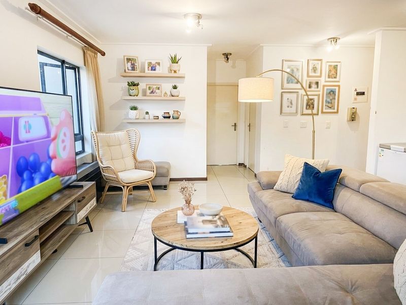 A bright and well-maintained living room featuring neutral tiled flooring, floating wall shelves, and modern recessed lighting, creating a comfortable and inviting atmosphere.